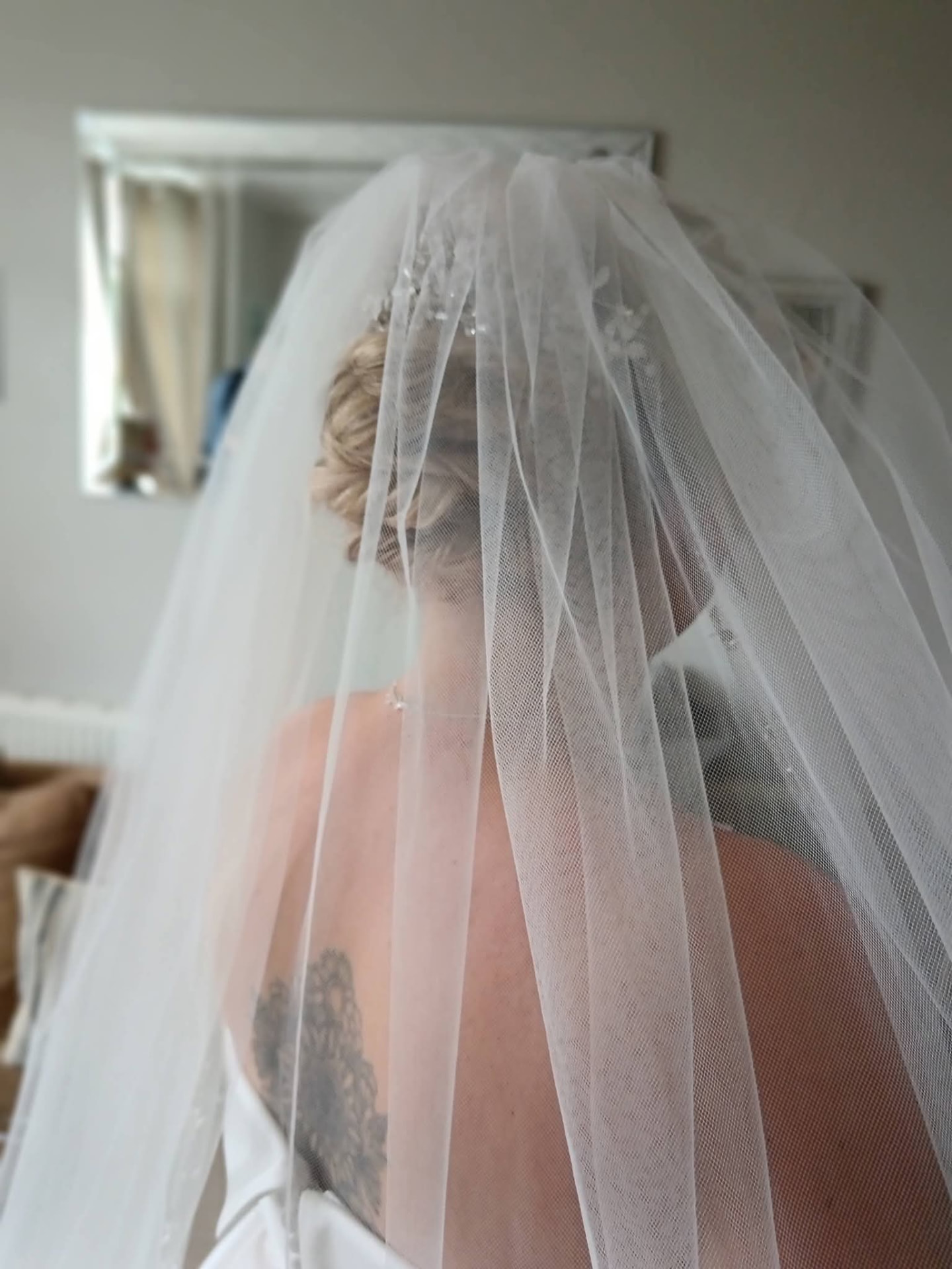 Back view of a bridal updo with a white floral hairpiece beneath a sheer veil